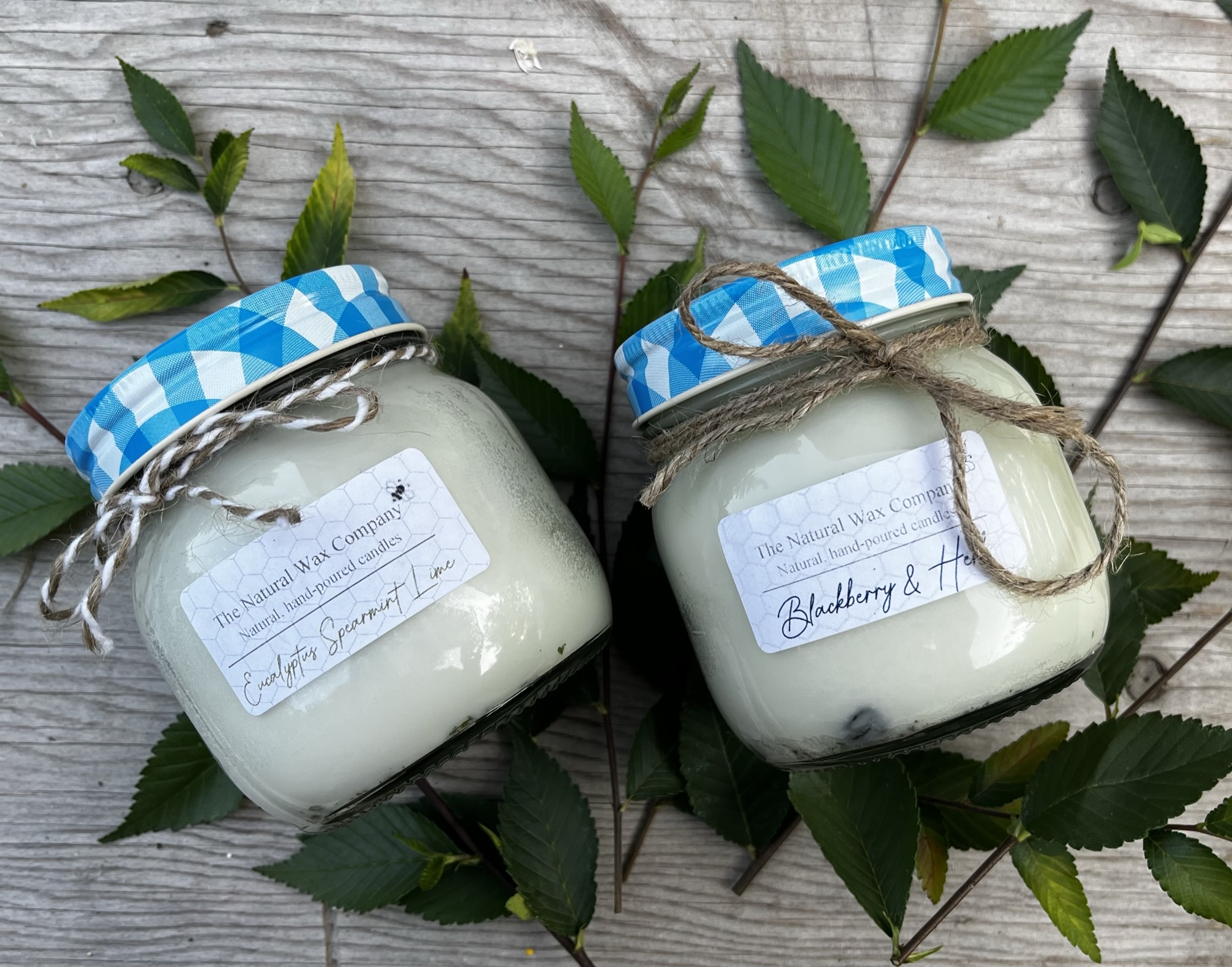 2 soy wax candles with blue lids. One is scented Eucalyptus spearmint lime, and the other is blackberry and herb